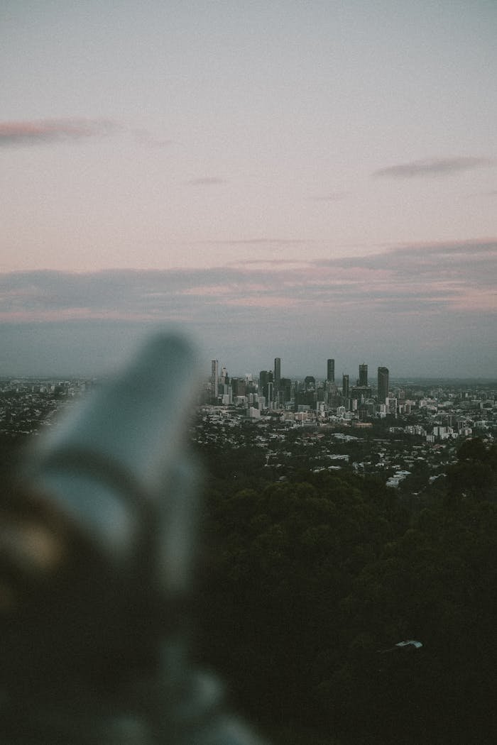 gallery-04 A scenic view of Brisbane's skyline at twilight, captured with a telescope in the foreground.